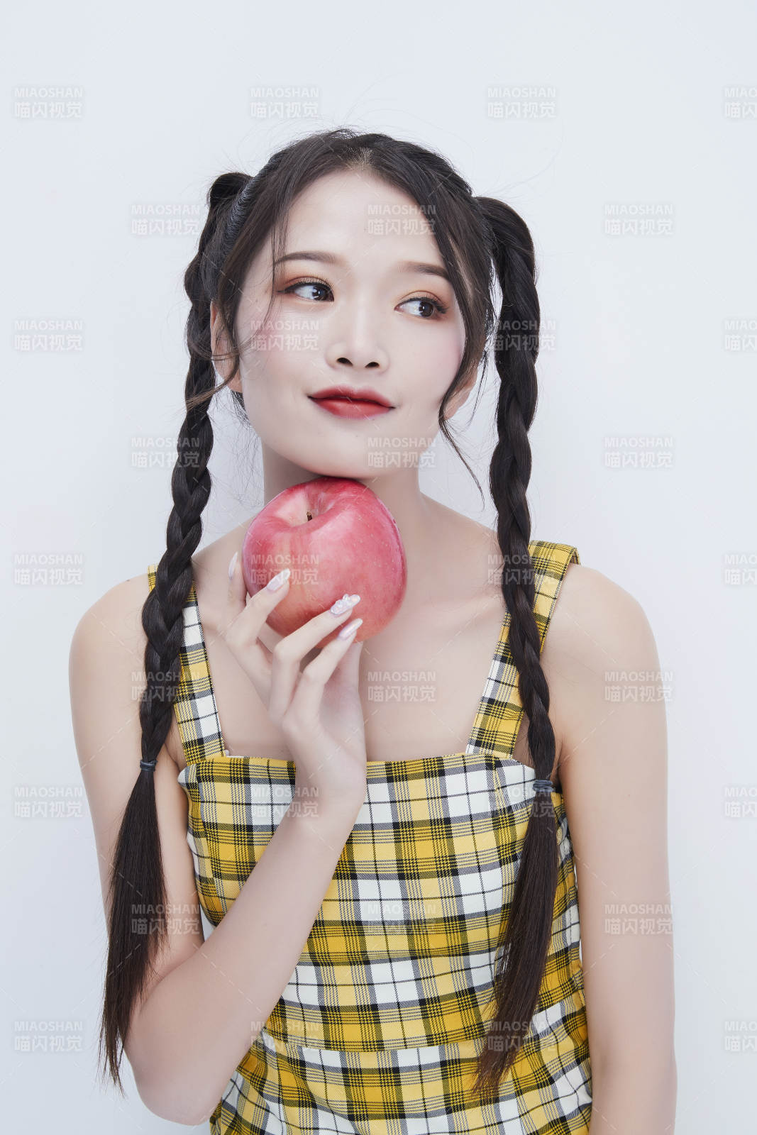 手拿苹果身穿格子吊带裙的亚洲可爱少女人像图片