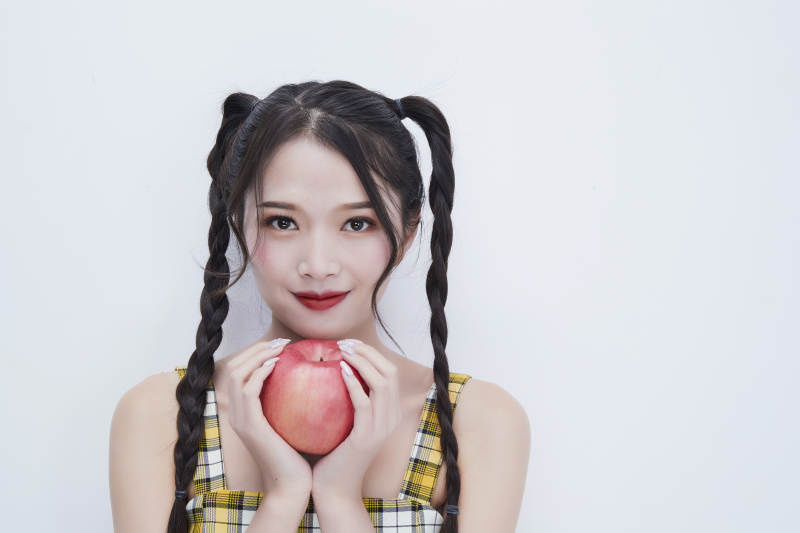 手拿苹果身穿格子吊带裙的亚洲可爱少女人像图片