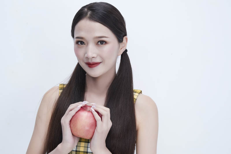 手拿苹果身穿格子吊带裙的亚洲可爱少女人像图片