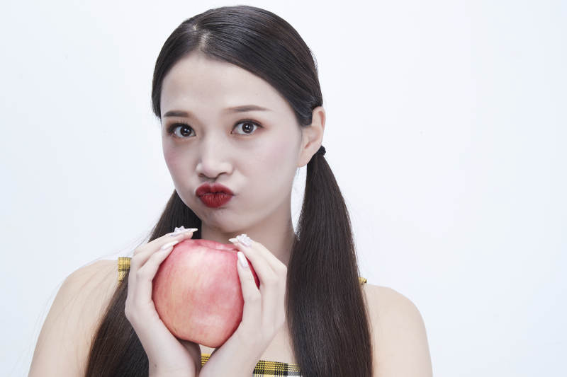 手拿苹果身穿格子吊带裙的亚洲可爱少女人像图片