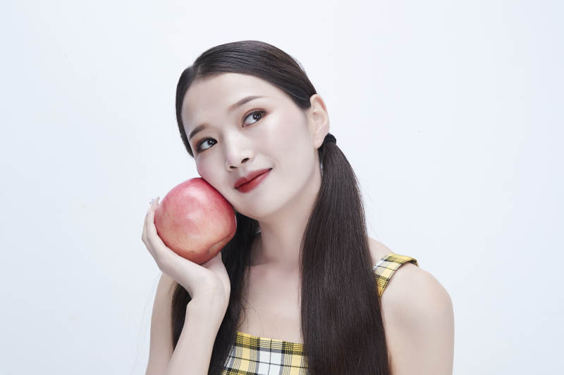 手拿苹果身穿格子吊带裙的亚洲可爱少女人像图片