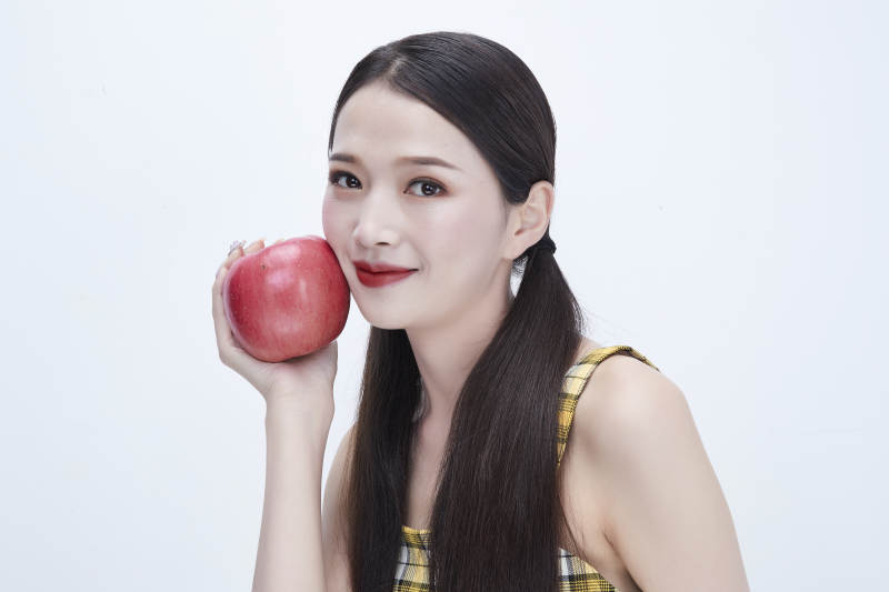 手拿苹果身穿格子吊带裙的亚洲可爱少女人像图片