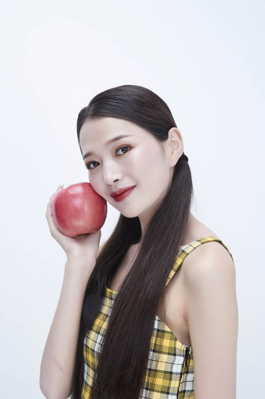 手拿苹果身穿格子吊带裙的亚洲可爱少女人像图片
