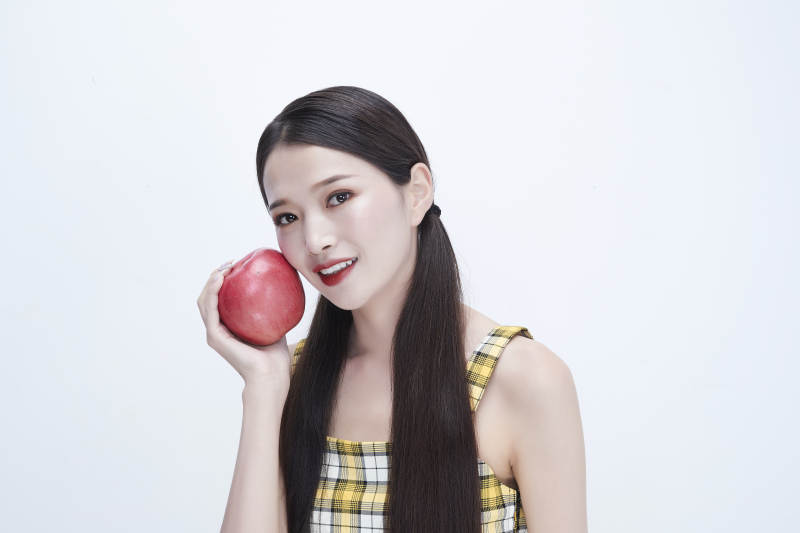 手拿苹果身穿格子吊带裙的亚洲可爱少女人像图片