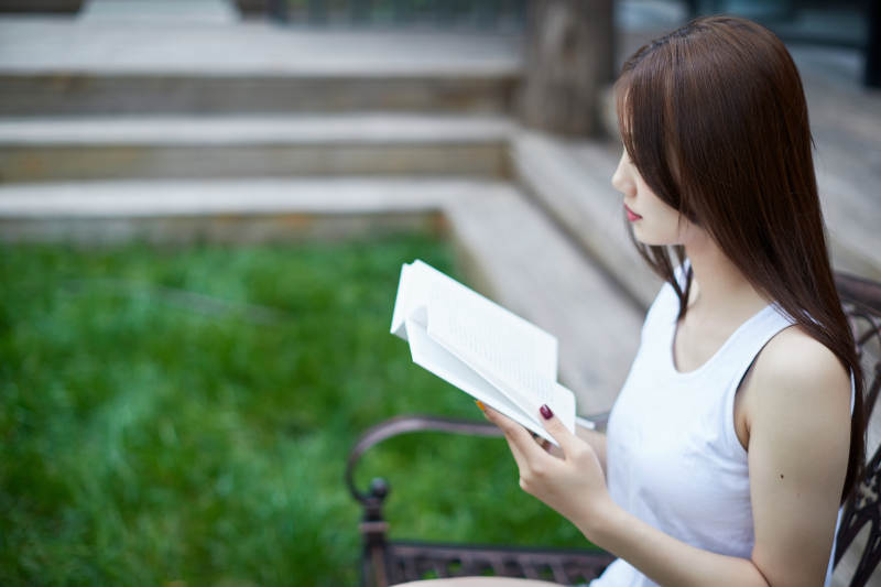 院子里坐在长椅上阅读书籍的亚洲长发少女图片