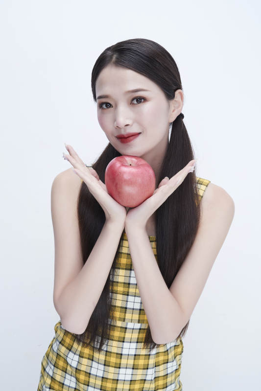 手拿苹果身穿格子吊带裙的亚洲可爱少女人像图片