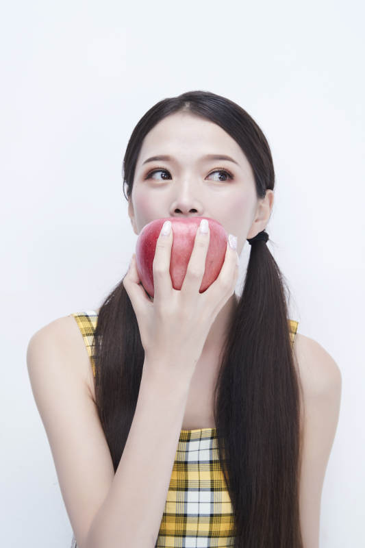 手拿苹果身穿格子吊带裙的亚洲可爱少女人像图片