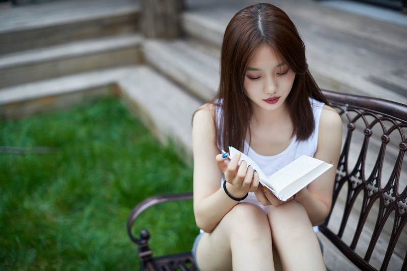 院子里坐在长椅上阅读书籍的亚洲长发少女图片