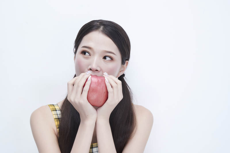 手拿苹果身穿格子吊带裙的亚洲可爱少女人像图片