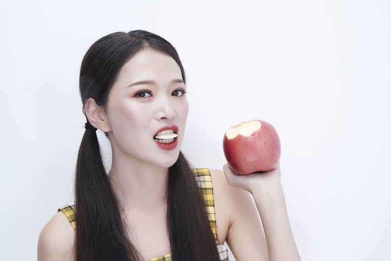 手拿苹果身穿格子吊带裙的亚洲可爱少女人像图片