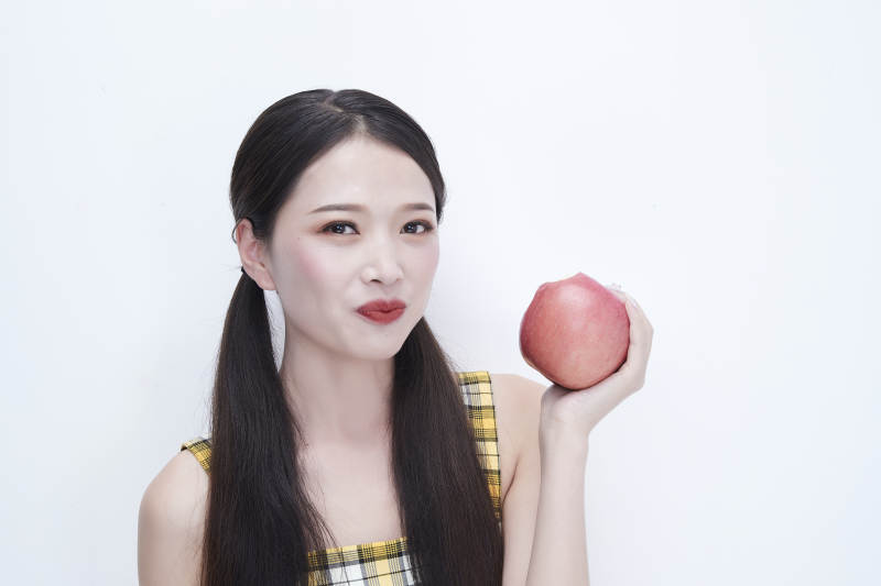手拿苹果身穿格子吊带裙的亚洲可爱少女人像图片