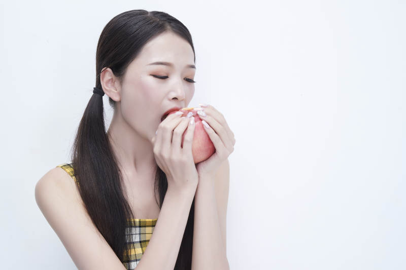 手拿苹果身穿格子吊带裙的亚洲可爱少女人像图片