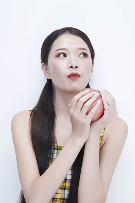 手拿苹果身穿格子吊带裙的亚洲可爱少女人像图片
