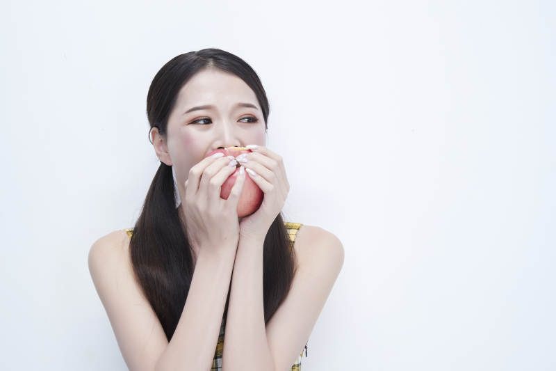 手拿苹果身穿格子吊带裙的亚洲可爱少女人像图片