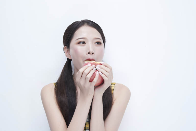 手拿苹果身穿格子吊带裙的亚洲可爱少女人像图片