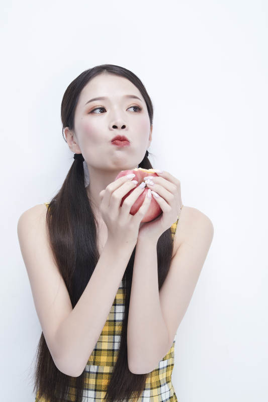 手拿苹果身穿格子吊带裙的亚洲可爱少女人像图片