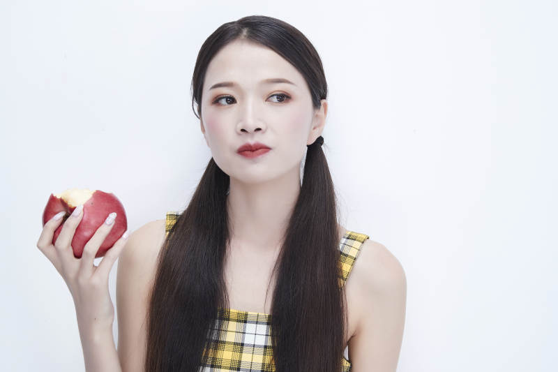 手拿苹果身穿格子吊带裙的亚洲可爱少女人像图片