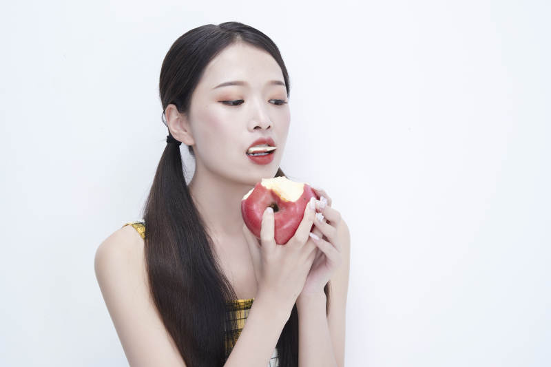 手拿苹果身穿格子吊带裙的亚洲可爱少女人像图片