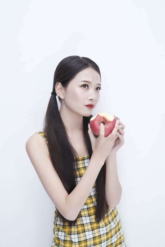 手拿苹果身穿格子吊带裙的亚洲可爱少女人像图片