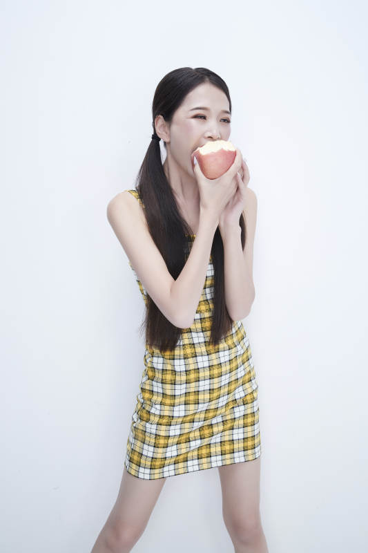 手拿苹果身穿格子吊带裙的亚洲可爱少女人像图片