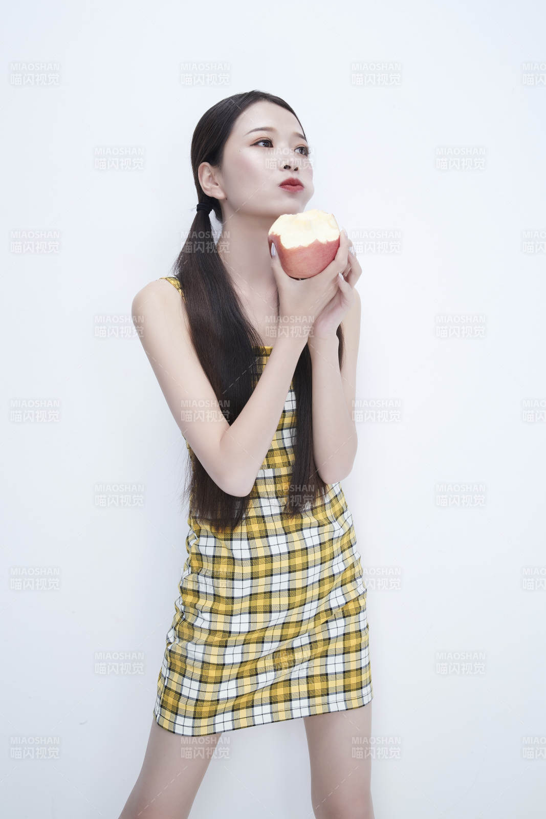 手拿苹果身穿格子吊带裙的亚洲可爱少女人像图片