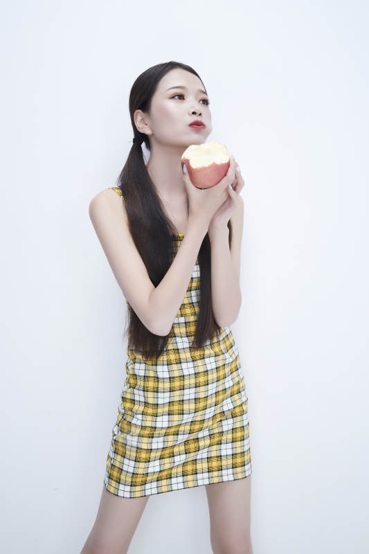 手拿苹果身穿格子吊带裙的亚洲可爱少女人像图片