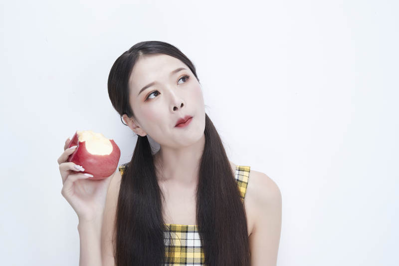 手拿苹果身穿格子吊带裙的亚洲可爱少女人像图片