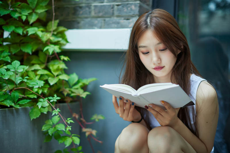 院子里坐在长椅上阅读书籍的亚洲长发少女图片