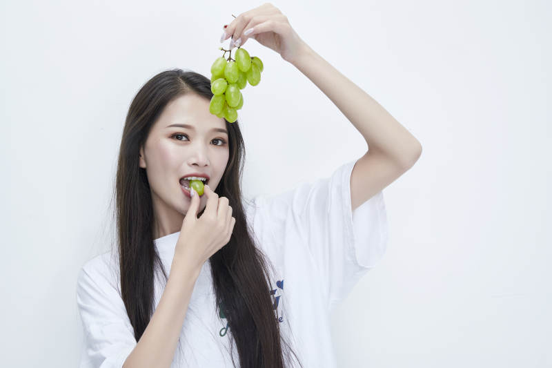 吃葡萄的穿白色长T血衫的长发可爱少女人像图片
