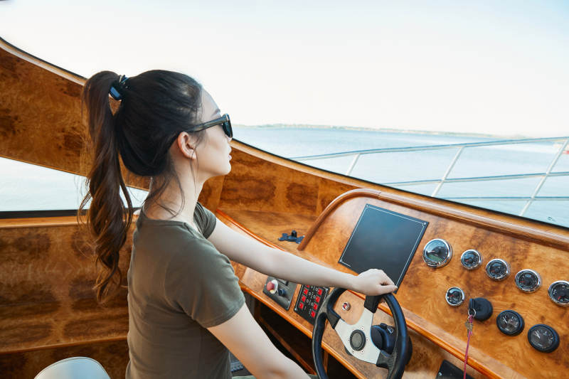 在海上戴着墨镜驾驶游艇的亚洲少女图片