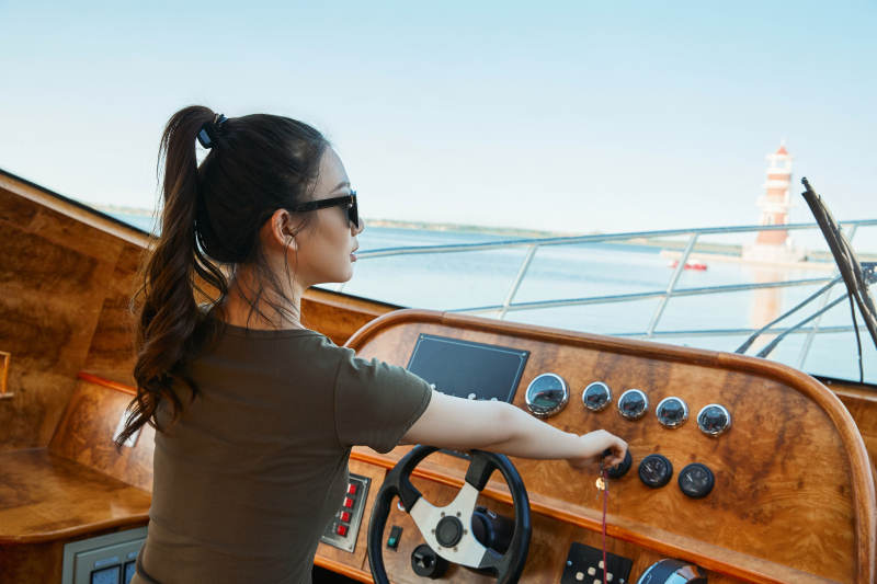 在海上戴着墨镜驾驶游艇的亚洲少女图片