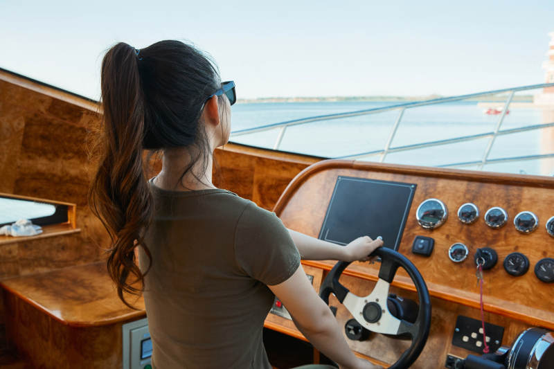 在海上戴着墨镜驾驶游艇的亚洲少女图片