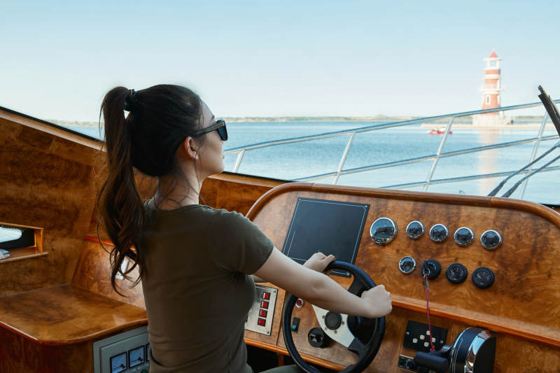 在海上戴着墨镜驾驶游艇的亚洲少女图片