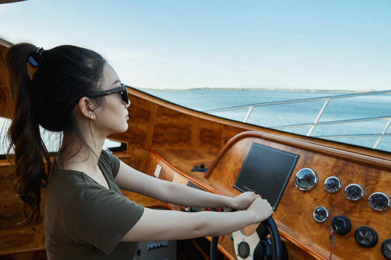 在海上戴着墨镜驾驶游艇的亚洲少女图片