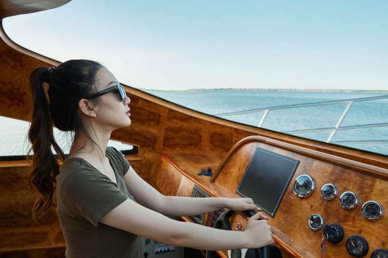 在海上戴着墨镜驾驶游艇的亚洲少女图片