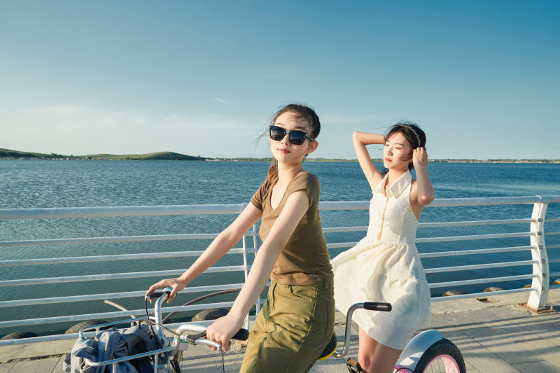 夕阳下湖边码头骑双人脚踏车的闺蜜少女图片