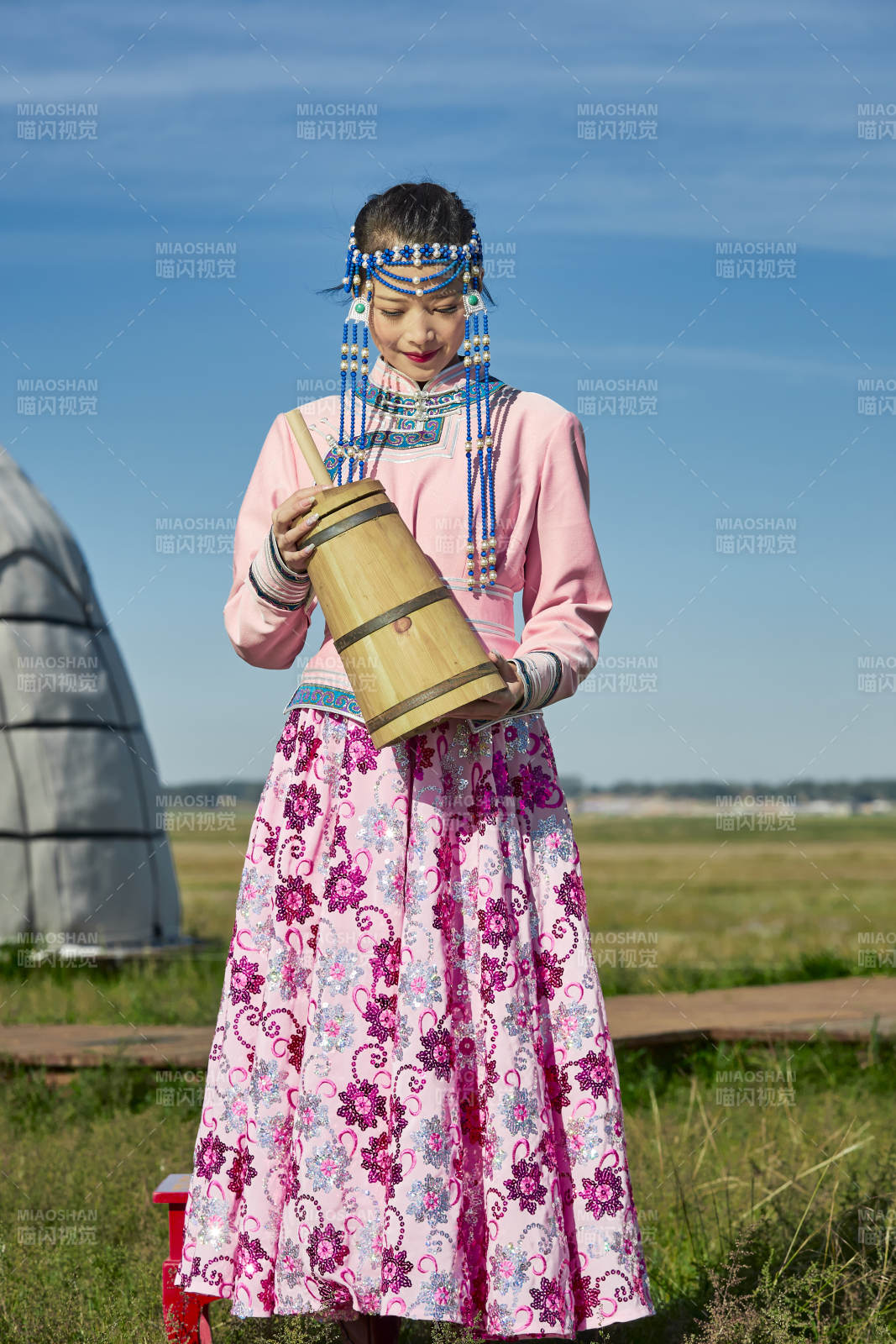 蒙古包前穿蒙古族饰怀抱奶茶桶的蒙族少女图片