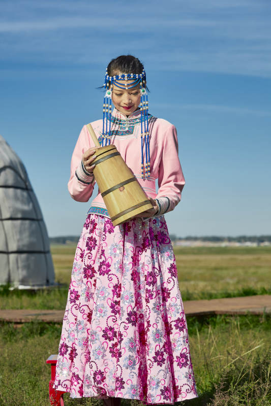 蒙古包前穿蒙古族饰怀抱奶茶桶的蒙族少女图片