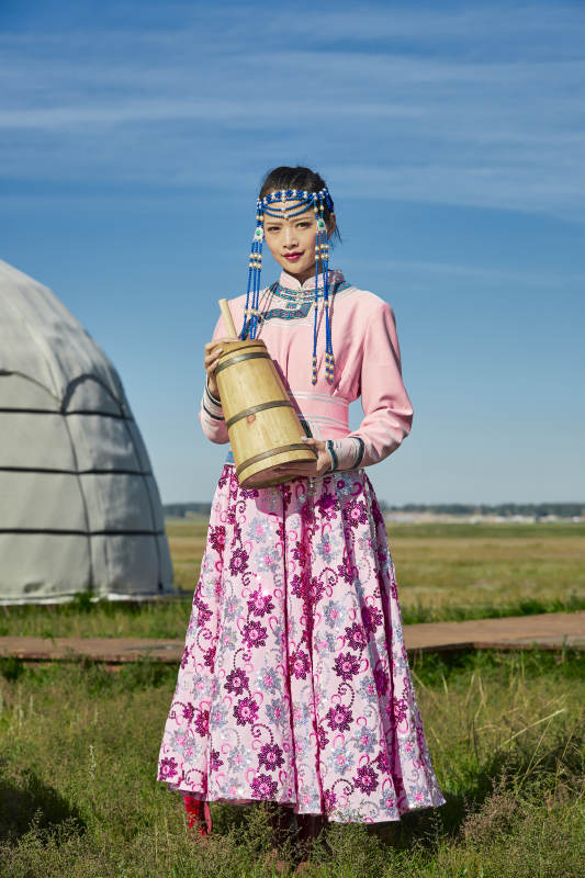 蒙古包前穿蒙古族饰怀抱奶茶桶的蒙族少女图片