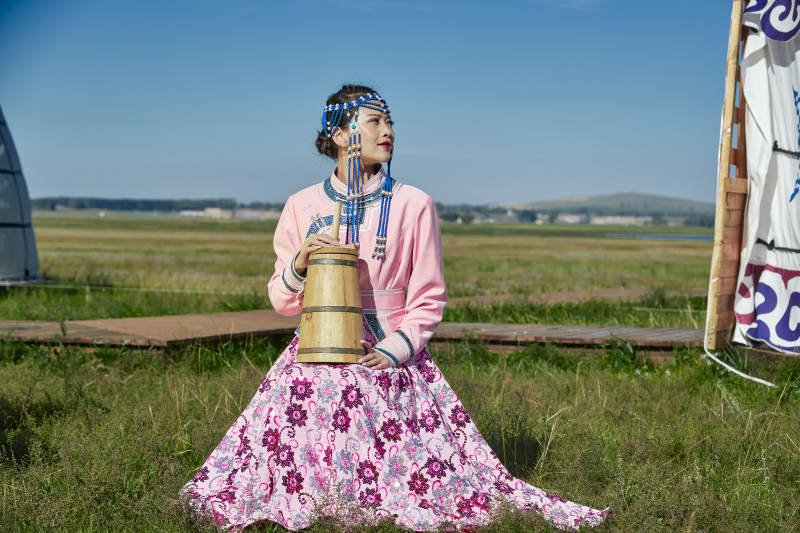 蒙古包前穿蒙古族饰怀抱奶茶桶的蒙族少女图片