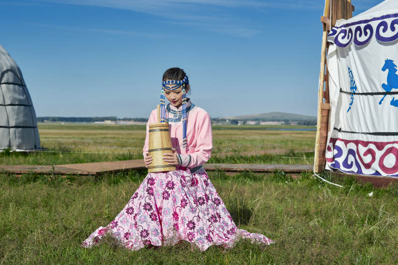 蒙古包前穿蒙古族饰怀抱奶茶桶的蒙族少女图片