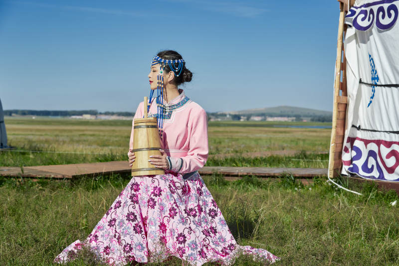 蒙古包前穿蒙古族饰怀抱奶茶桶的蒙族少女图片