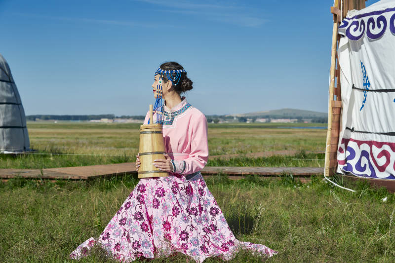 蒙古包前穿蒙古族饰怀抱奶茶桶的蒙族少女图片