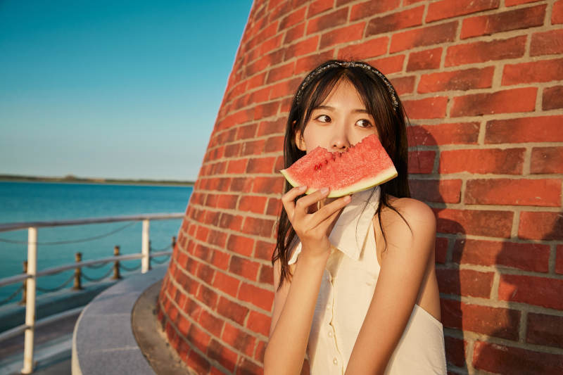 盛夏夕阳湖边码头灯塔上吃西瓜的少女图片