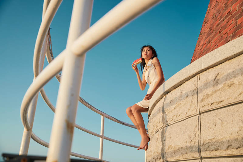 盛夏夕阳湖边码头灯塔上吃西瓜的少女图片