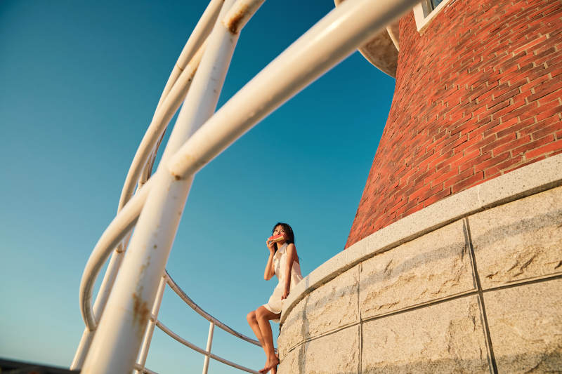 盛夏夕阳湖边码头灯塔上吃西瓜的少女图片