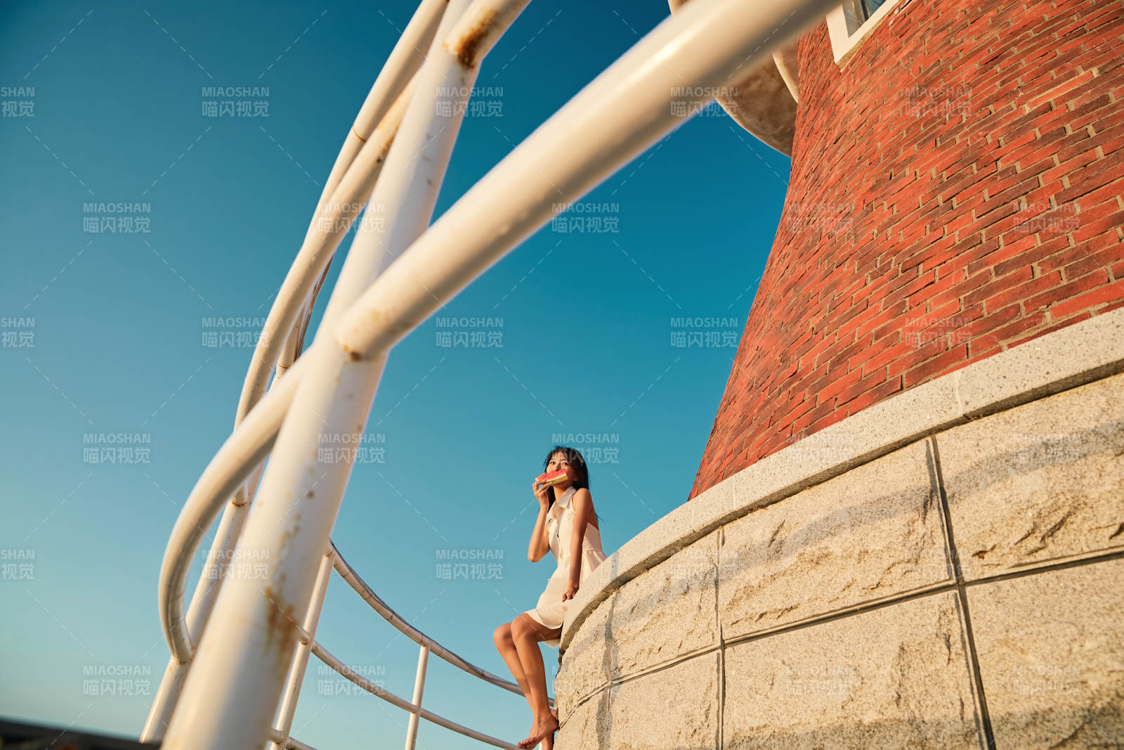 盛夏夕阳湖边码头灯塔上吃西瓜的少女图片