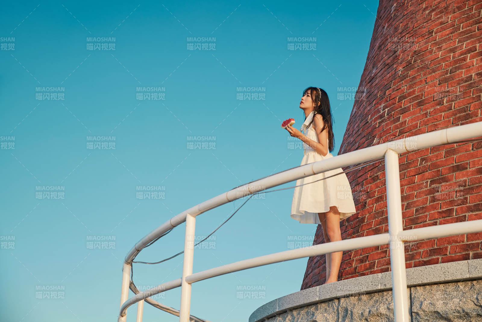 盛夏夕阳湖边码头灯塔上吃西瓜的少女图片