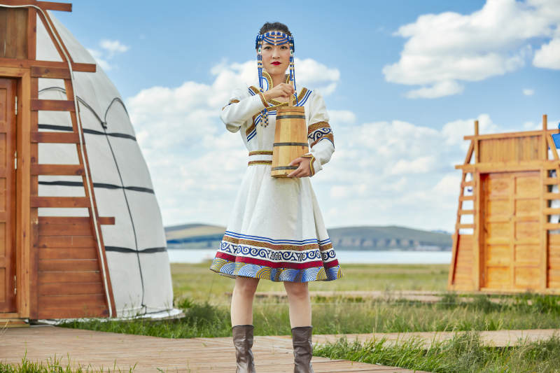 蒙古包前穿蒙古族饰怀抱奶茶桶的蒙族少女图片