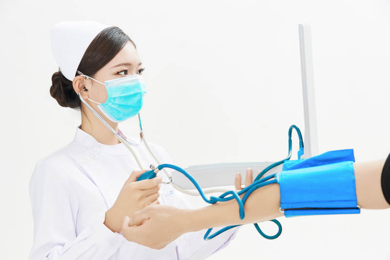 白色背景下手持血压计为患者测量血压的护士图片